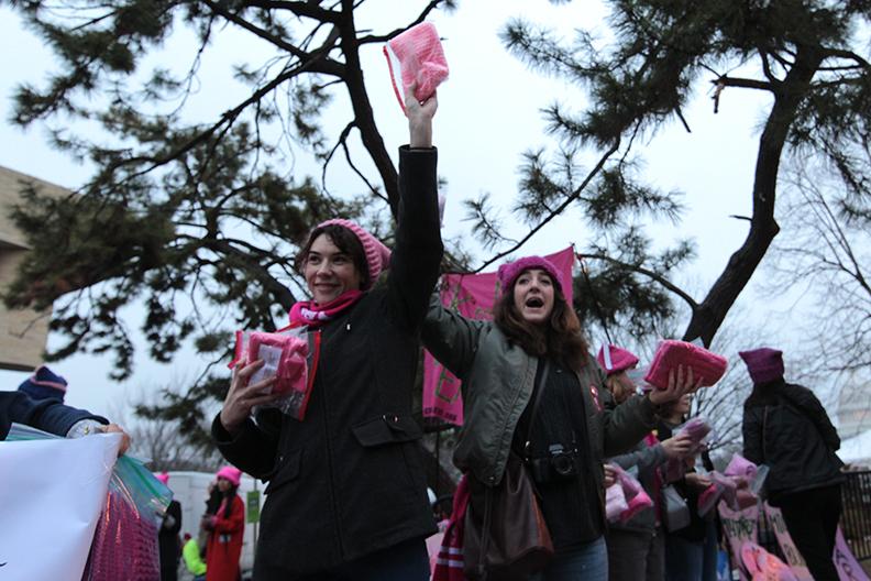 Julie Buisson of France (left) and Jane Cody of Maryland (right) hand out hats as part of the Pussyhat Project at the Womens March. Photo by Lu Gerdemann.
