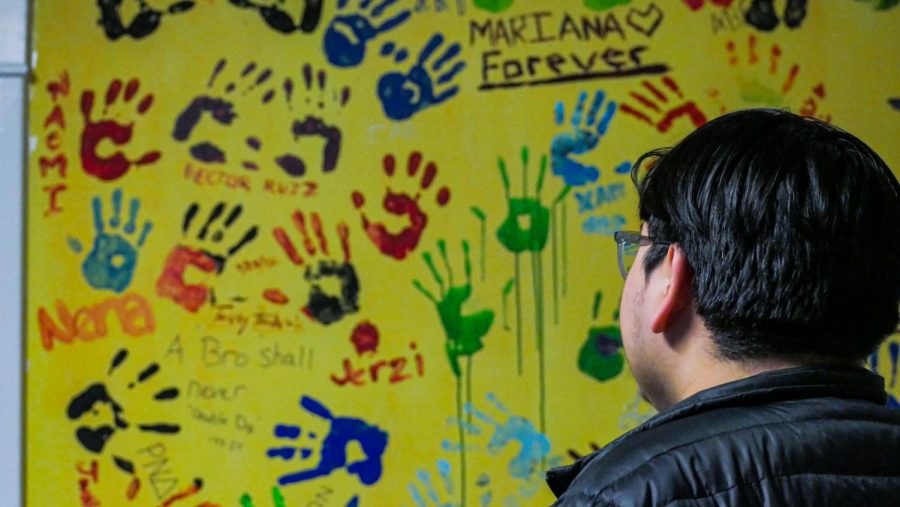 Latinx Unidos president, Anthony Silva, watches the hand prints on Casa Latina’s wall mural of former members.